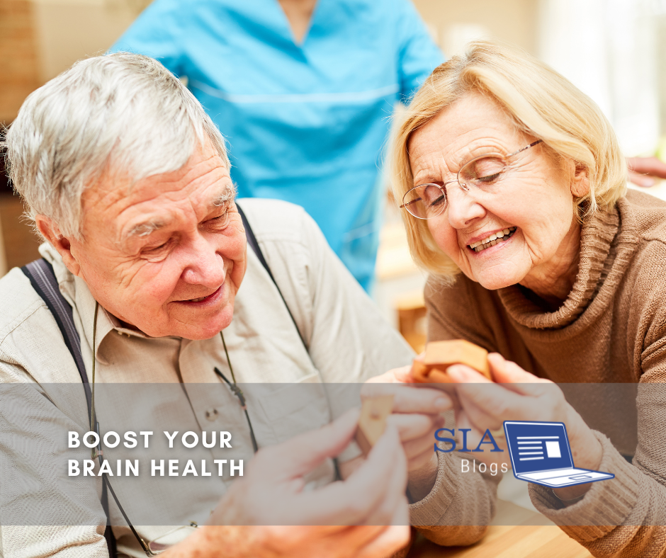 An elderly couple engages in a fun activity together, with the woman smiling and holding a small object while the man looks on. A healthcare worker is seen in the background, contributing to a warm, supportive environment.