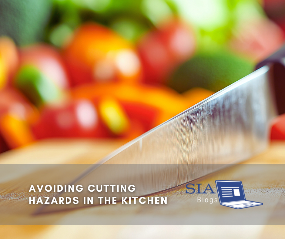 A close-up of a sharp kitchen knife on a wooden cutting board with blurred, colorful vegetables in the background. The image conveys a focus on kitchen safety and cutting hazards.